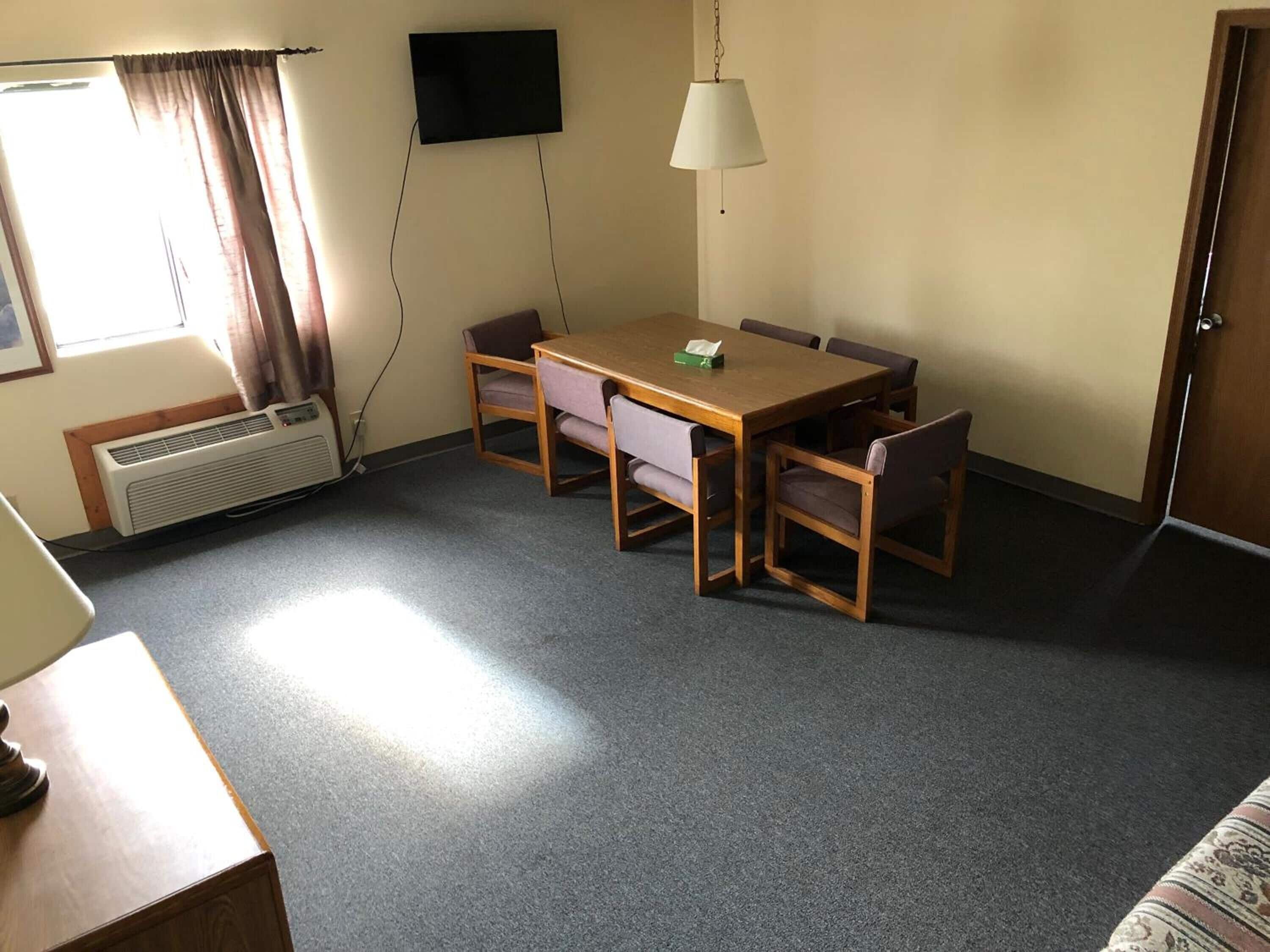 Una habitación con una mesa y sillas de madera, un televisor de pantalla plana montado en la pared, una lámpara de techo y una puerta.