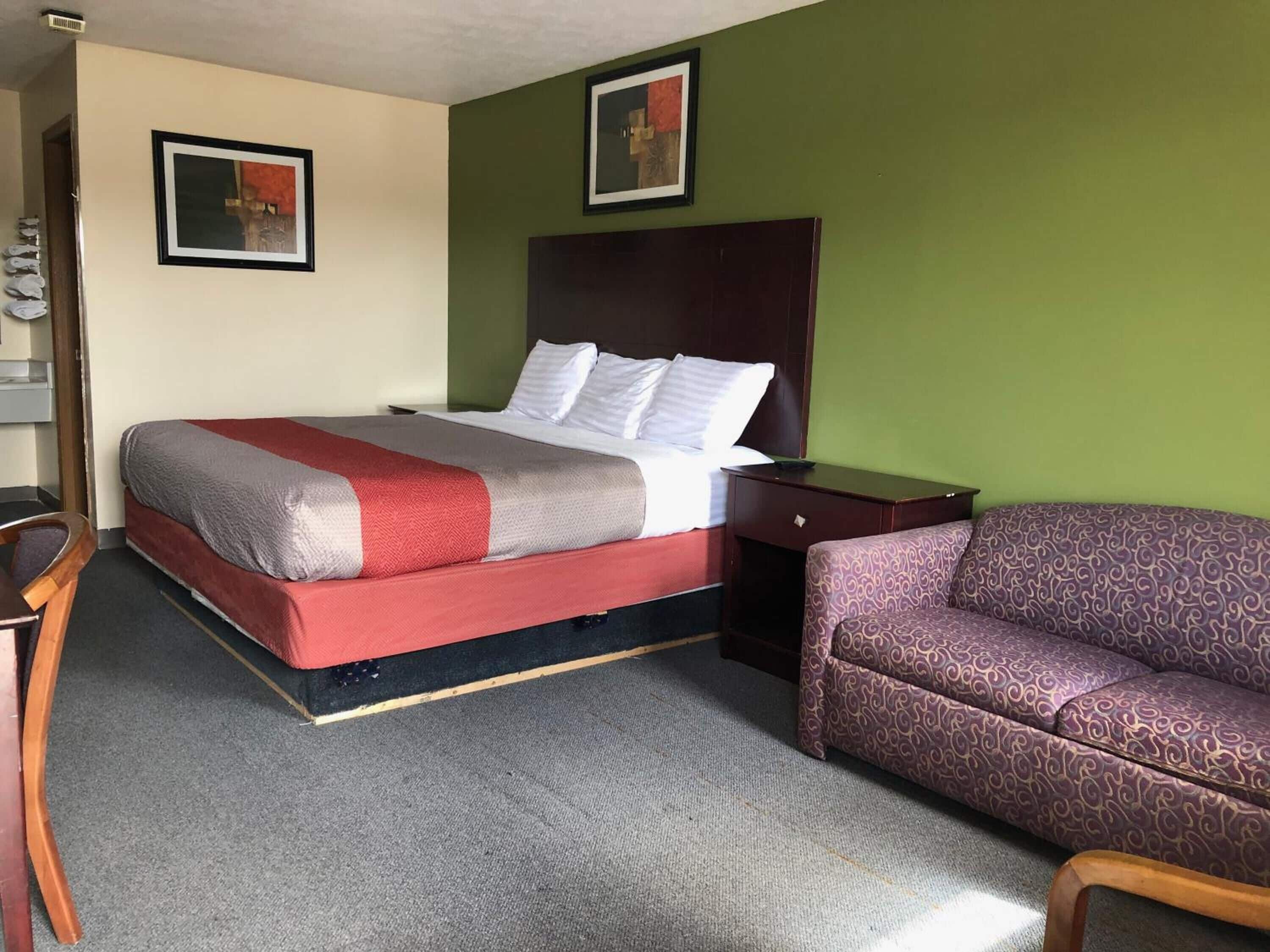 Et hotelværelse med en seng, et trænatbord, en stribet sofa og to billeder i rammer på væggene.