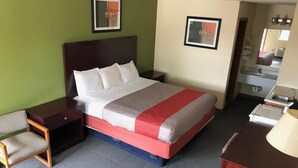 A hotel room with a bed, a desk, a chair, a dresser, and a mirror.