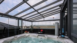 A hot tub with a glass enclosure, a bottle of champagne, and two glasses on a tray. - Mirage Medic Hotel (Budapest)