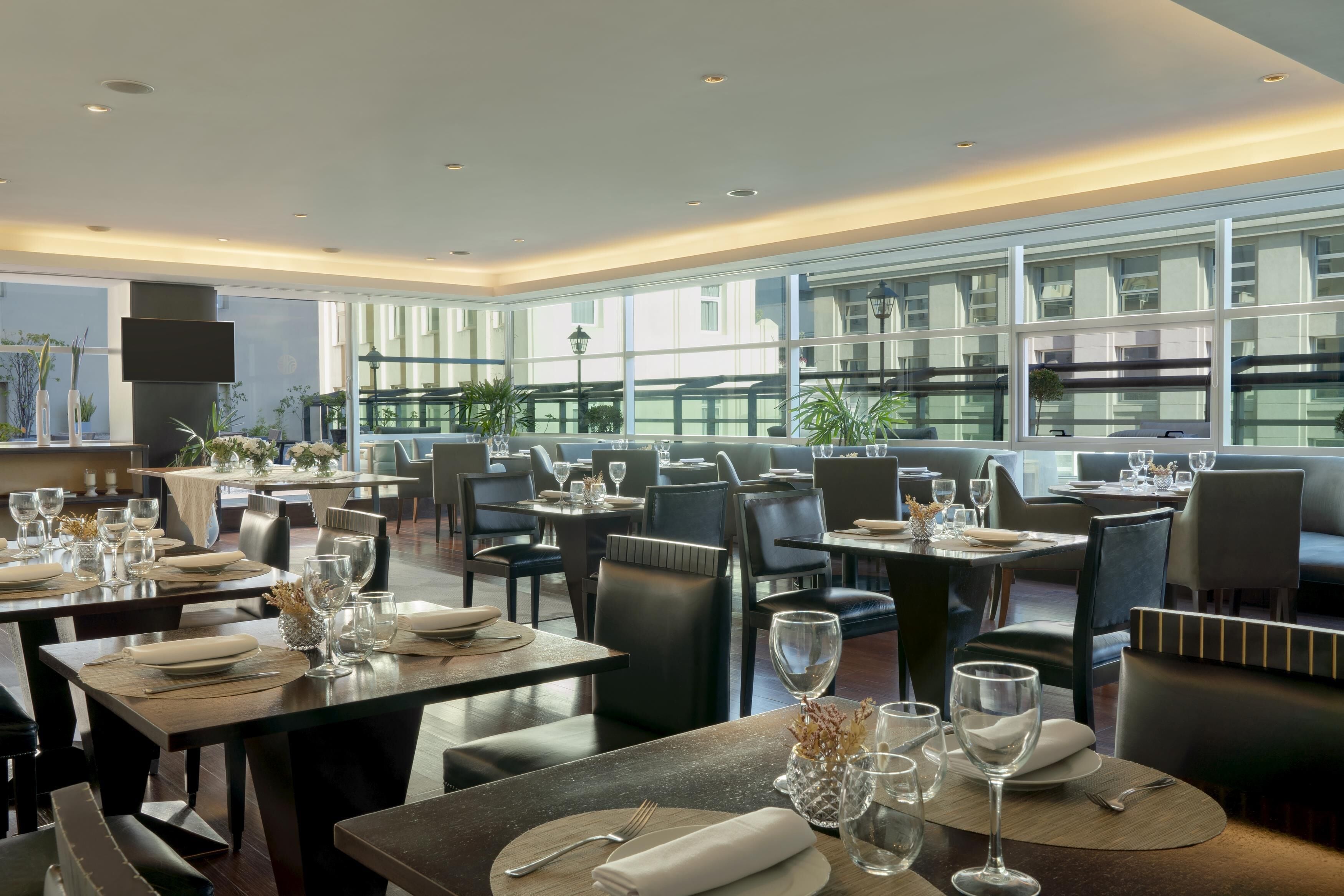 Un restaurant moderne doté de nombreuses tables, de chaises et d’une grande fenêtre offrant une vue sur la ville.