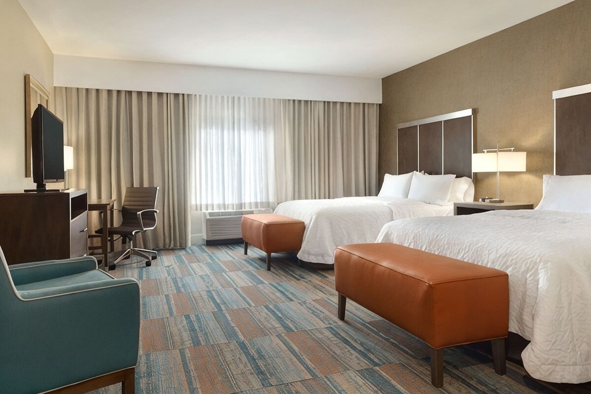 A hotel room with two beds, a desk, a chair, and a television.