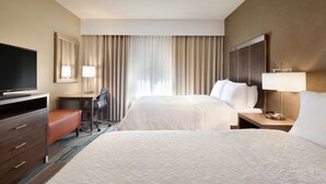 Habitación de hotel con dos camas, un escritorio, una silla, un televisor y un ventanal con cortinas.