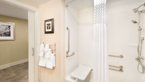 Een badkamer met een douche, handgrepen, een witte handdoekhouder en een lijst met een foto aan de muur.