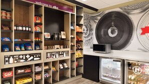 Zona de exhibición de bocadillos y bebidas, con diversas opciones de snacks empaquetados, bebidas en botella y una pantalla de televisión.