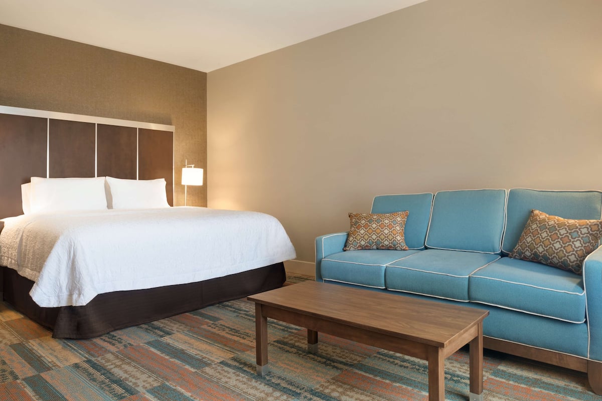 Quarto de hotel com cama, sofá azul e mesa de centro.