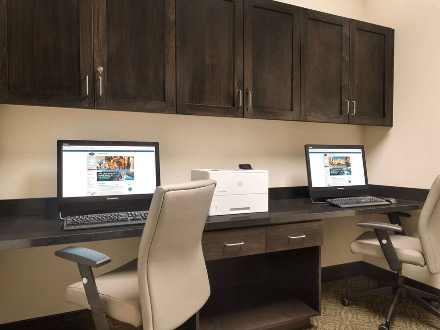 A dual-monitor workstation with two chairs, a printer, and dark wooden cabinets.