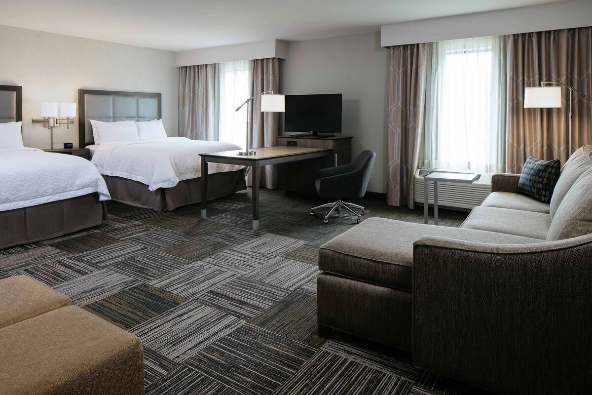 A hotel room with two beds, a desk with a TV, a sofa, and a small table.
