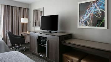 A hotel room with a bed, a desk with a flat-screen TV, a chair, a cabinet, and a large abstract painting on the wall.