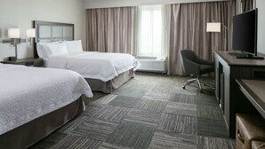A hotel room with two beds, a desk with a TV, a chair, and a large window with curtains. - Hampton Inn & Suites Hudson (Hudson)