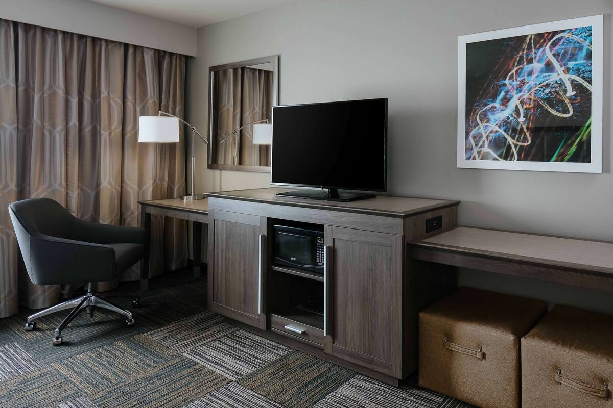A hotel room with a desk, a flat-screen TV, a chair, a microwave, and storage boxes.