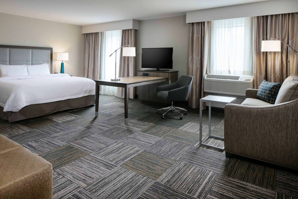A hotel room with a bed, desk, TV, and seating area.