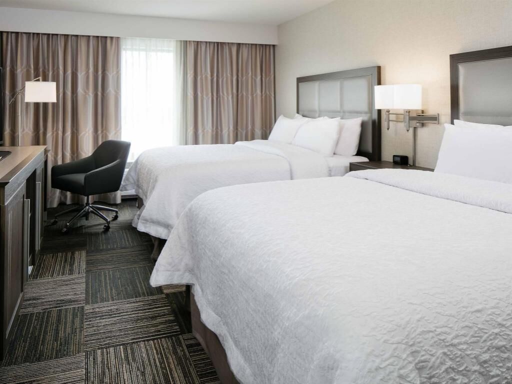 A hotel room with two beds, a desk, a chair, and a window with curtains.