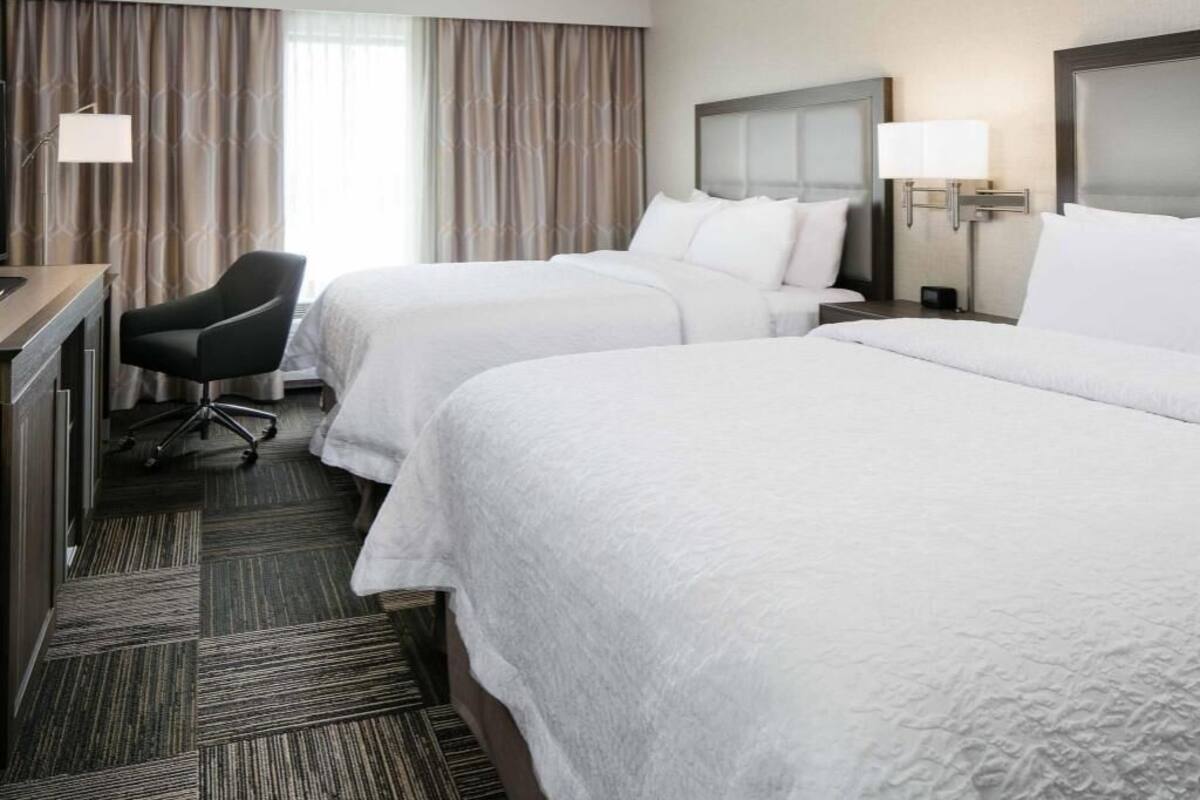 Habitación de hotel con dos camas, un escritorio, una silla y una ventana con cortinas.