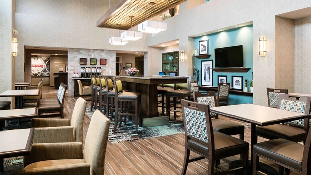 A hotel lobby with a bar area, seating arrangements, and a television. - Hampton Inn & Suites Hudson (Hudson)