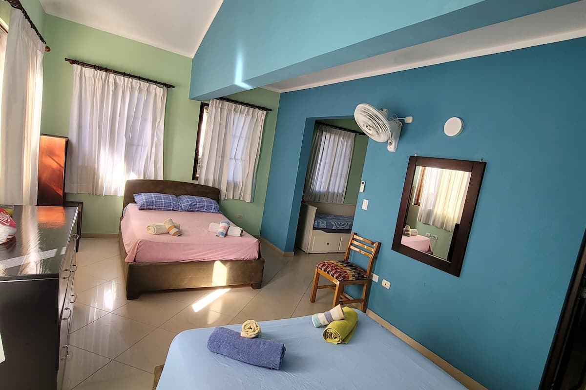 A hotel room with two beds, a desk, a chair, a mirror, and a ceiling fan.
