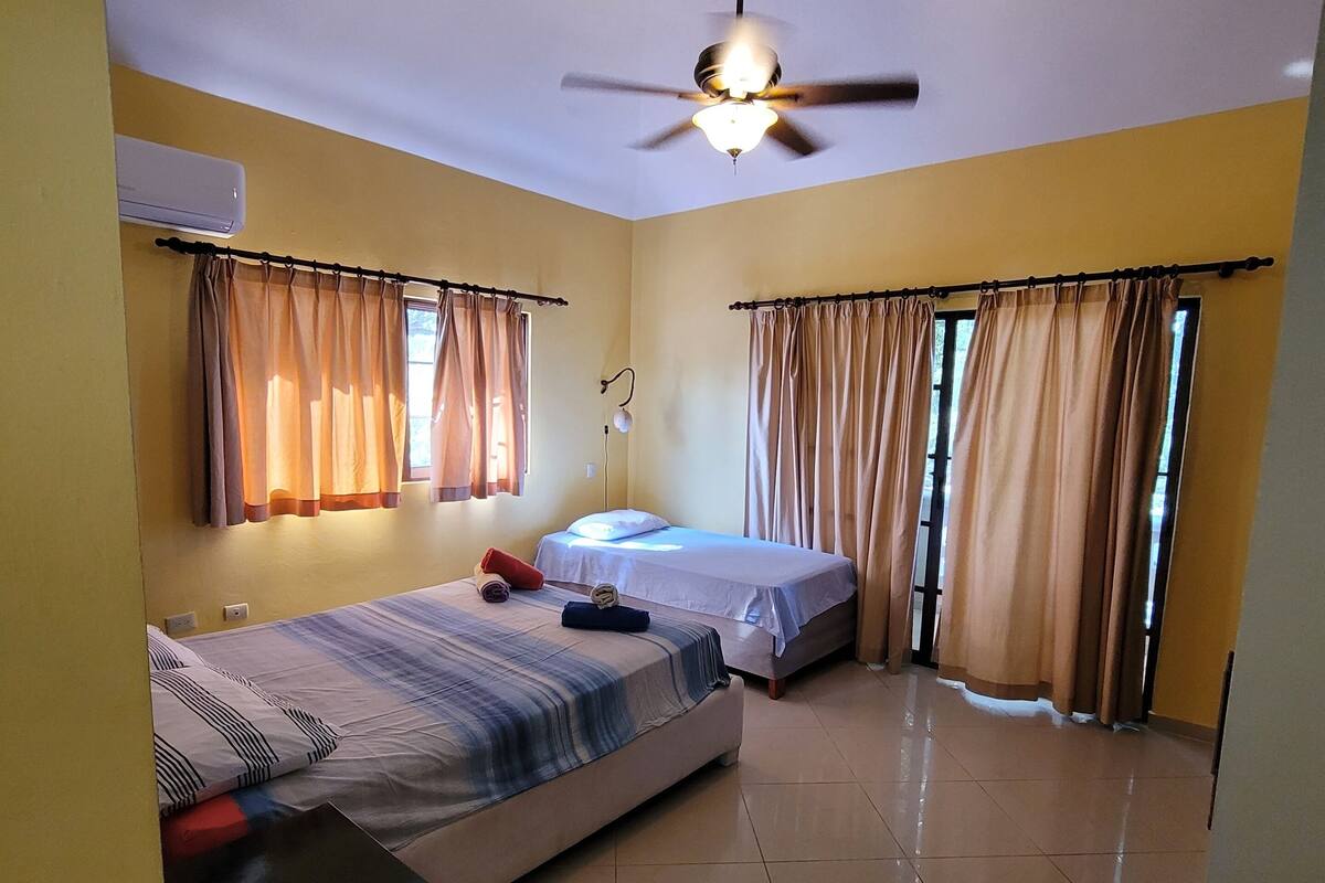 A room with two beds, a ceiling fan, and a window with curtains.