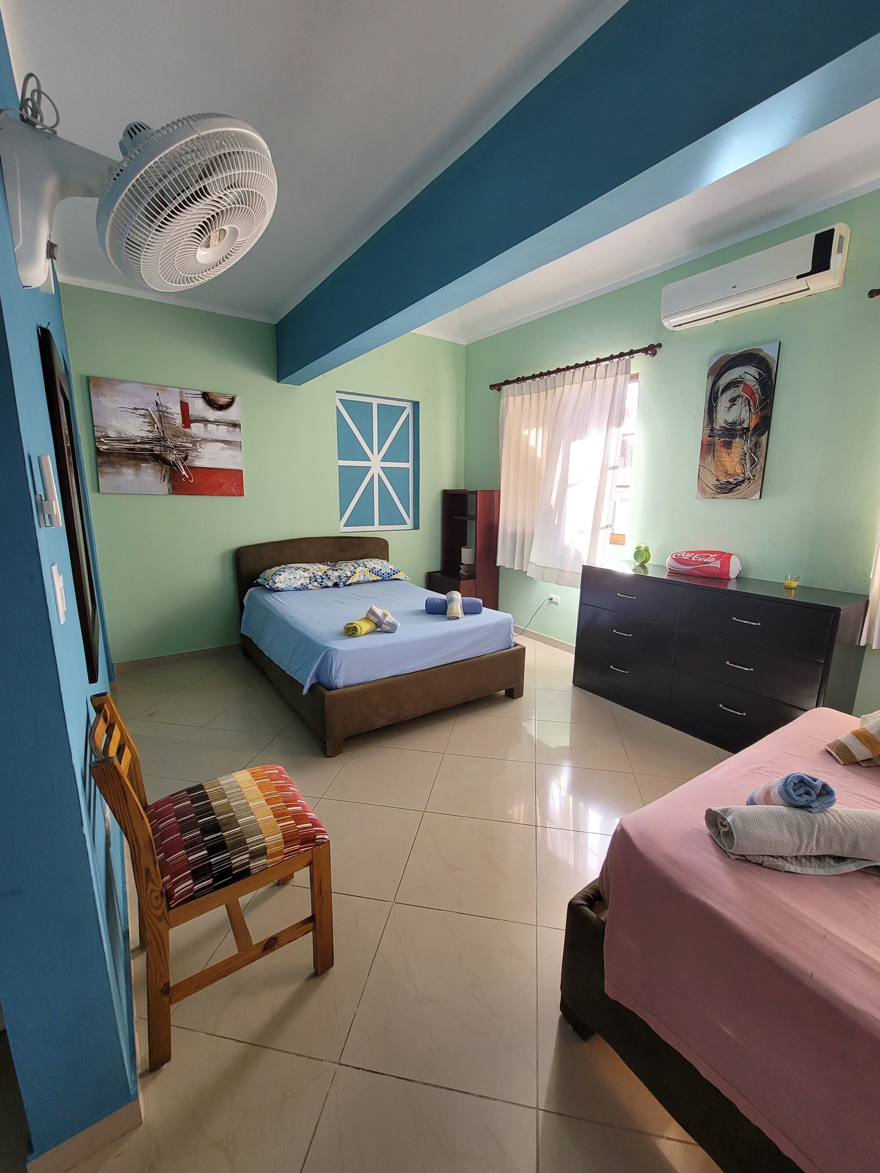 A bedroom with a bed, a chair, a dresser, and a fan.