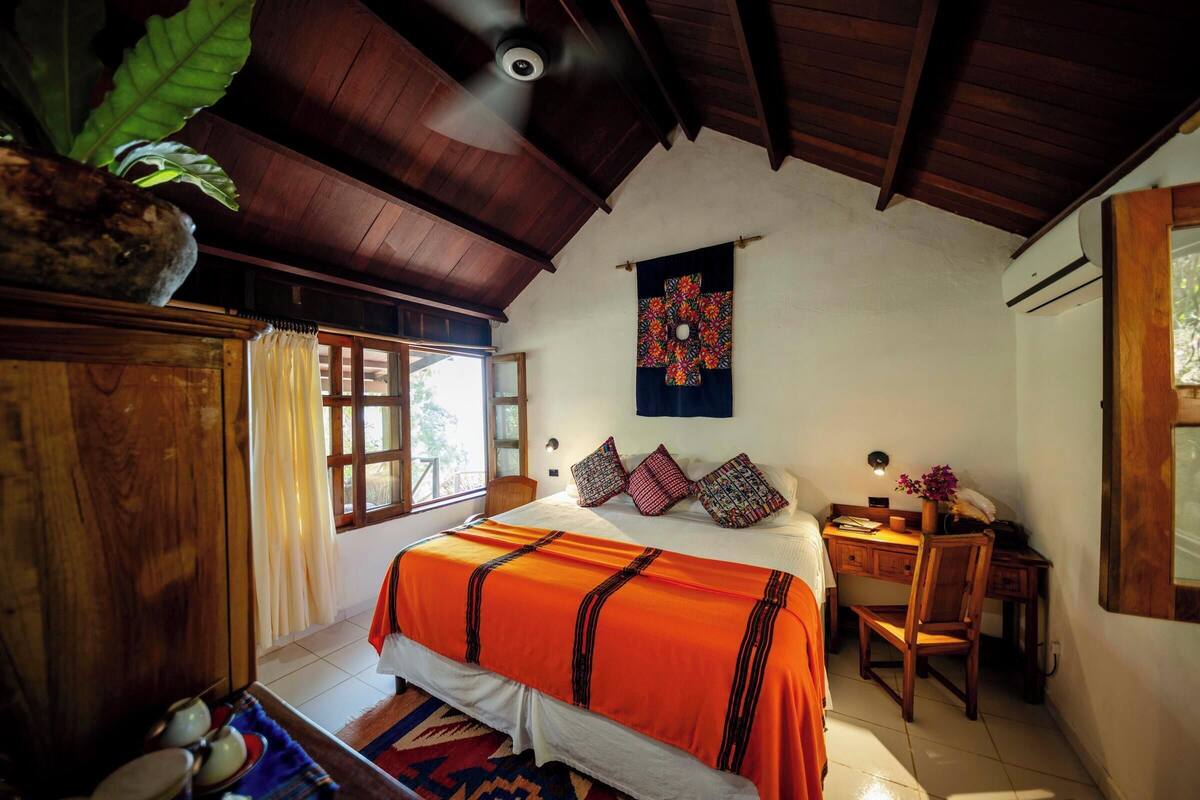 Un dormitorio con cama, escritorio, silla, ventana y ventilador de techo.