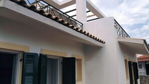A modern building with a flat roof, green shutters, and a stone wall. - Letos Villas (Paxos)