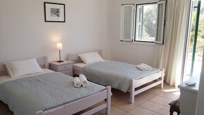 A twin bedroom with two beds, a bedside table with a lamp, a framed picture on the wall, and a window with curtains. - Letos Villas (Paxos)