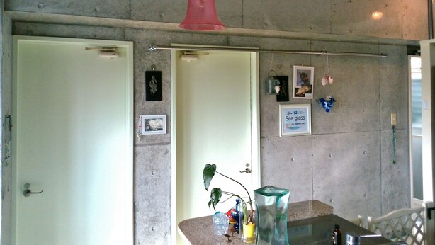 A room with a concrete wall, a red hanging light fixture, a framed picture, and a small potted plant on a counter. - Guest House Sea glass (Itoman)