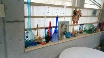Una exhibición de coloridos jarrones de cristal sobre una estantería en una habitación con suelo de hormigón y una ventana de diseño cuadriculado.