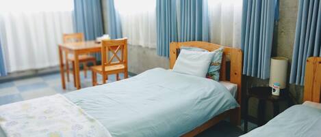 A hotel room with two beds, a wooden chair, a small table, and a lamp.