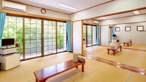 Een traditionele Japanse kamer met tatami vloerbedekking, schuifdeuren, een houten tafel, een televisie en een klein kastje.