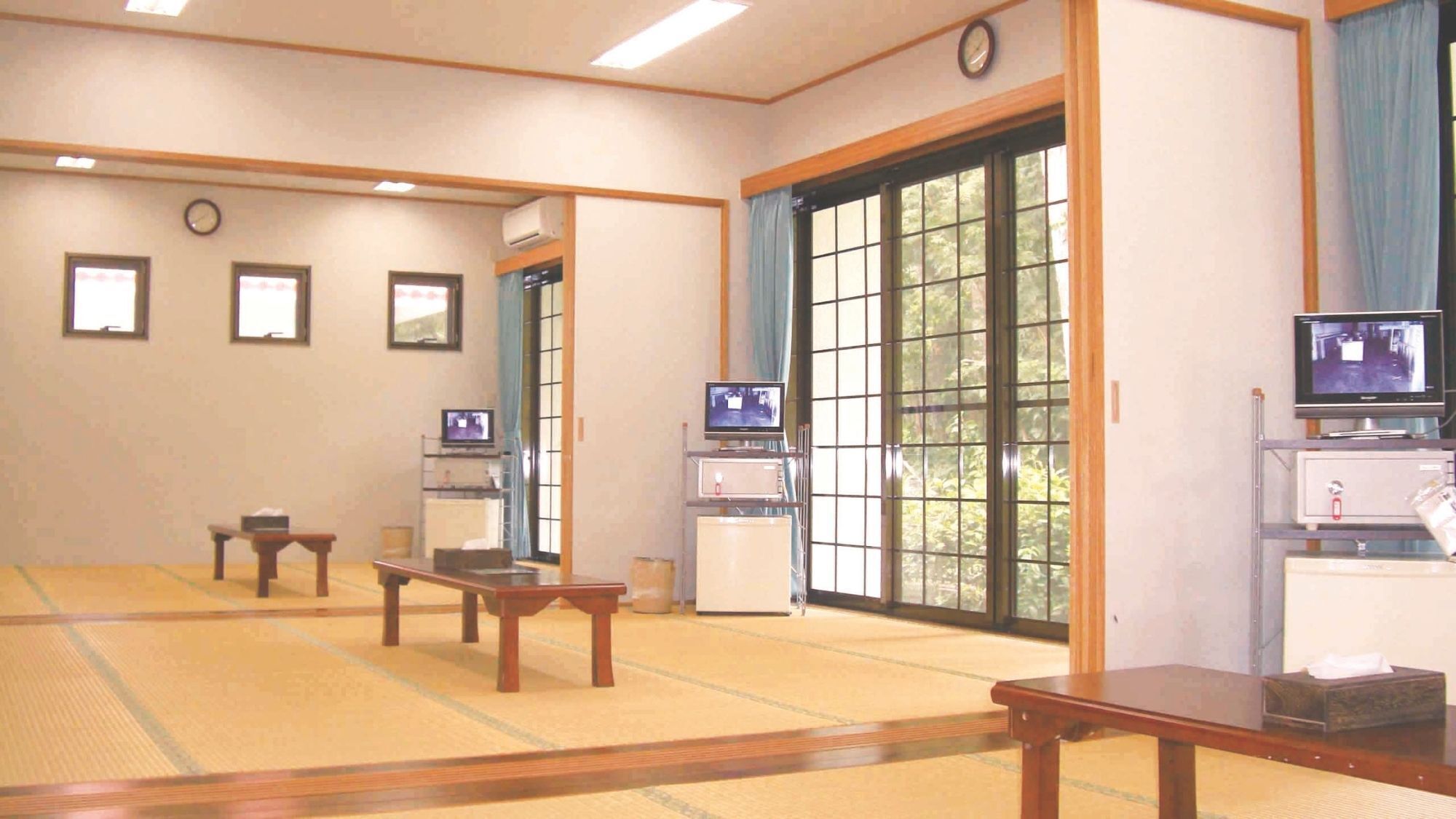 Une pièce de style japonais traditionnel, avec un sol recouvert de tatamis, des portes coulissantes et plusieurs téléviseurs.