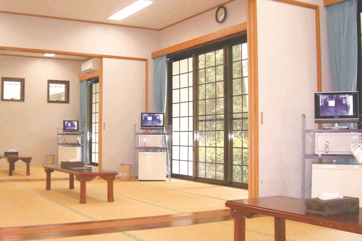 A traditional Japanese room with tatami flooring, sliding doors, and multiple televisions.