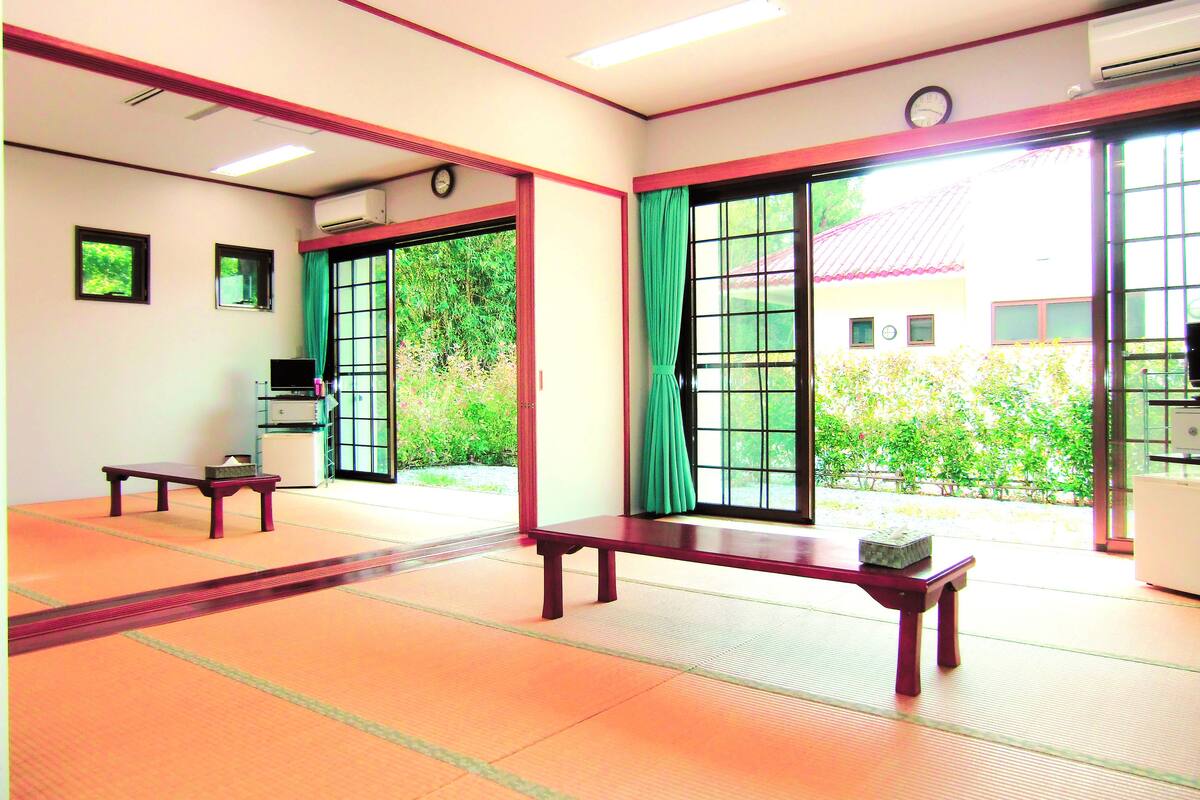 A traditional Japanese room with tatami flooring, a wooden bench, a small table, and a sliding door leading to a garden.