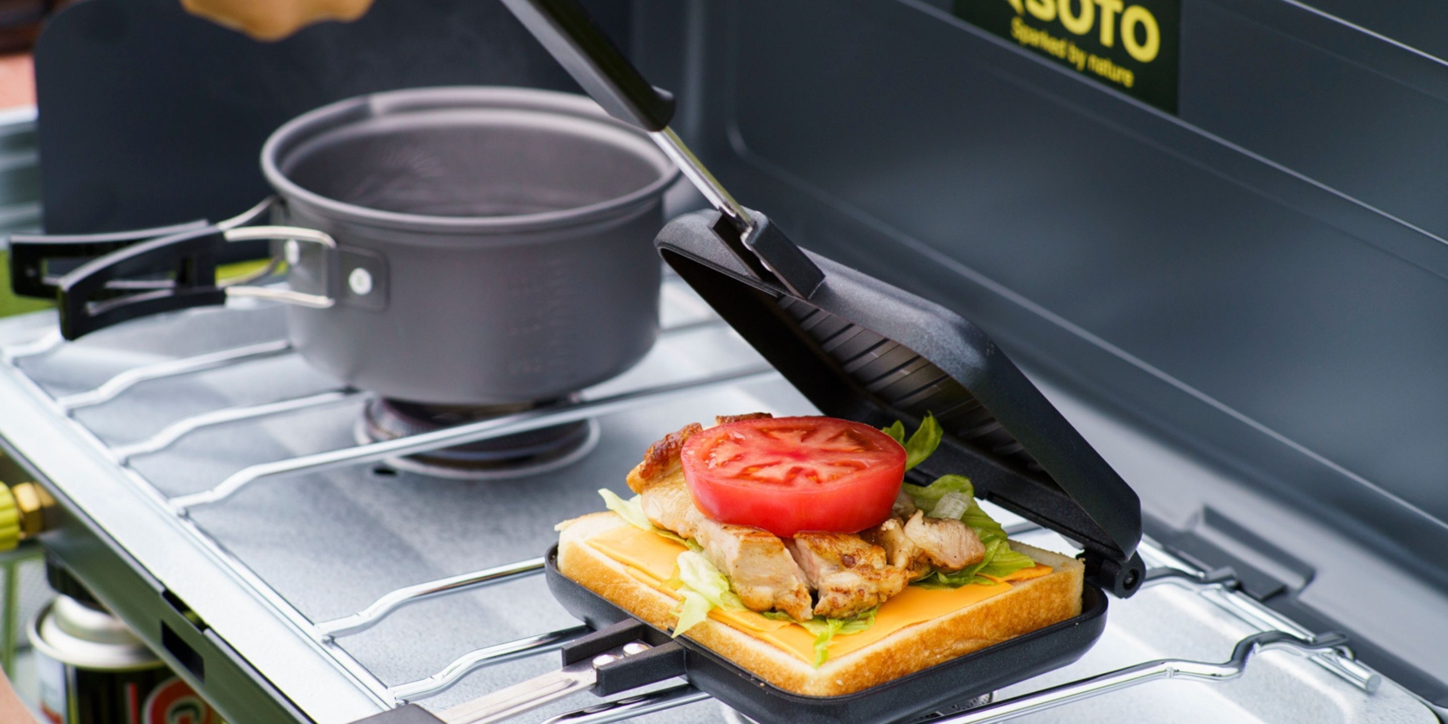 A sandwich on a portable grill with a pot in the background.