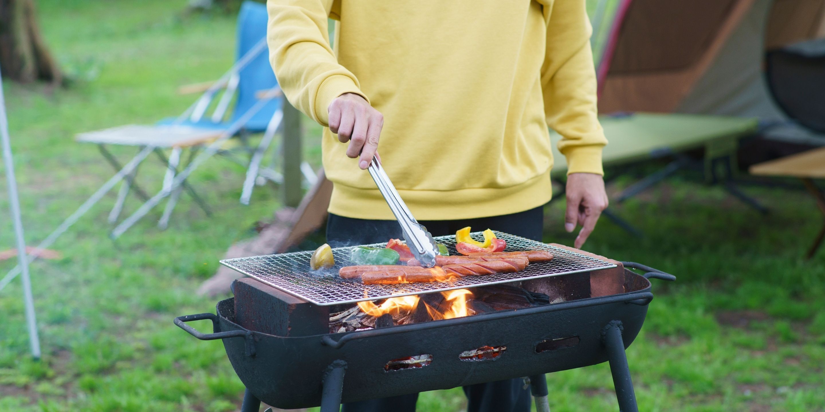 Iemand barbecuet worstjes op een buitenbarbecue.