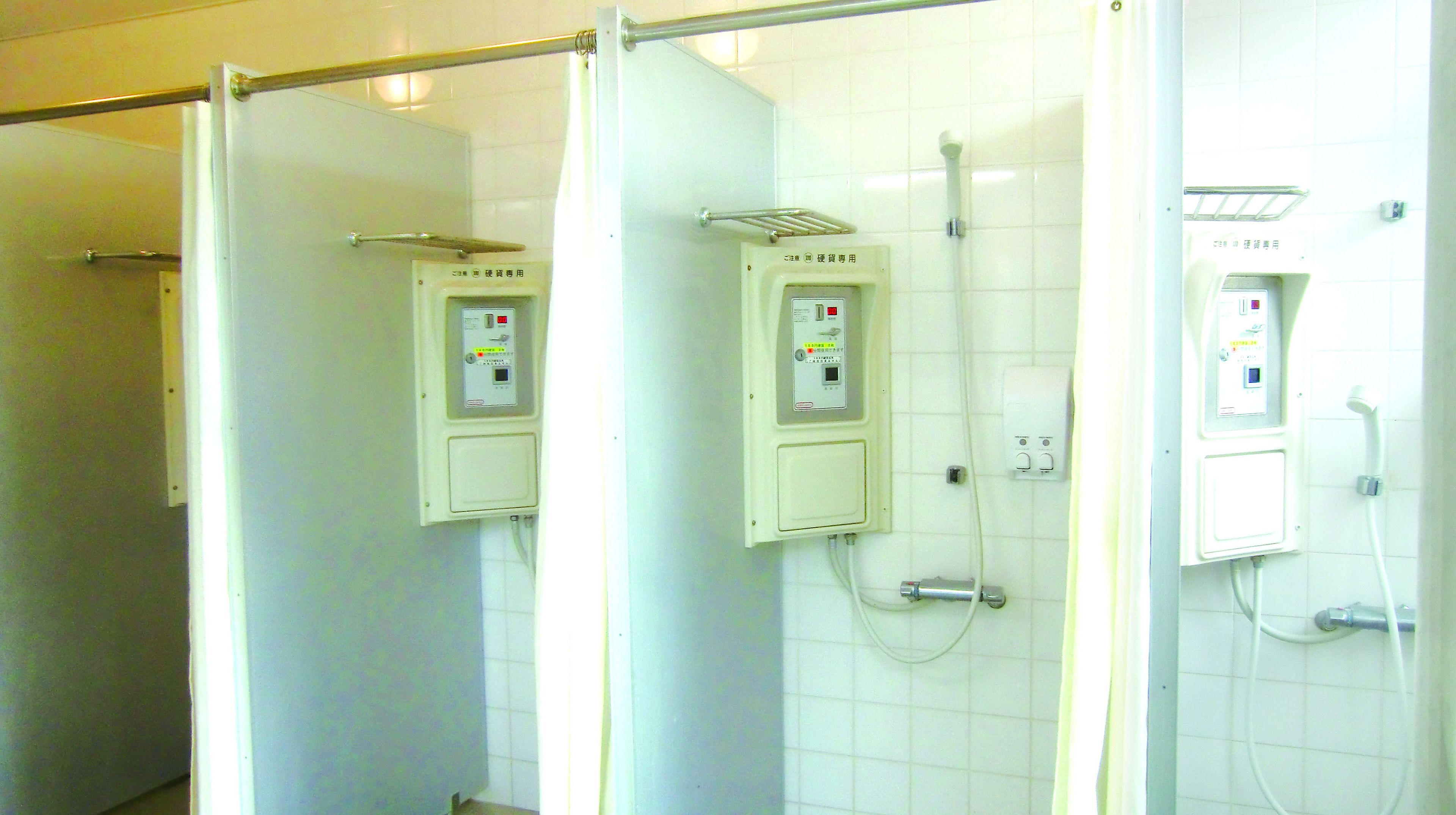 A public restroom with three shower stalls, each equipped with a control panel and a hand dryer.
