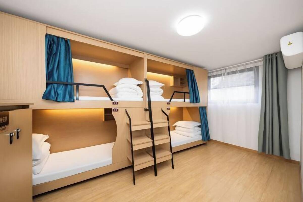 A compact hotel room with bunk beds, a wardrobe, and a window with curtains.