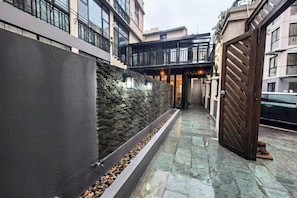 A narrow outdoor corridor with a stone wall on one side, a metal gate on the other, and a tiled floor.