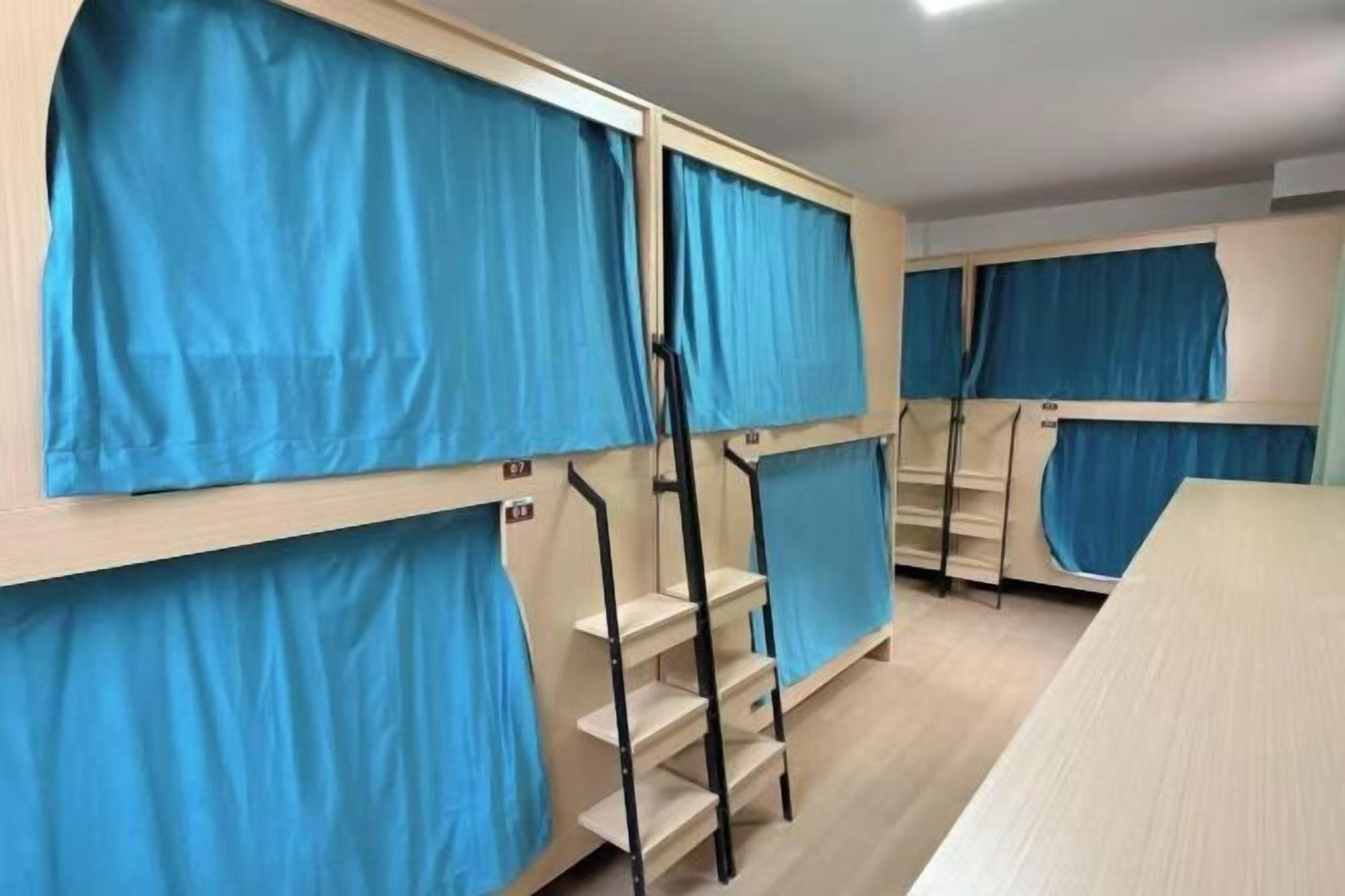 Un dormitorio con literas, cada una con una cortina azul, y un escritorio de madera.
