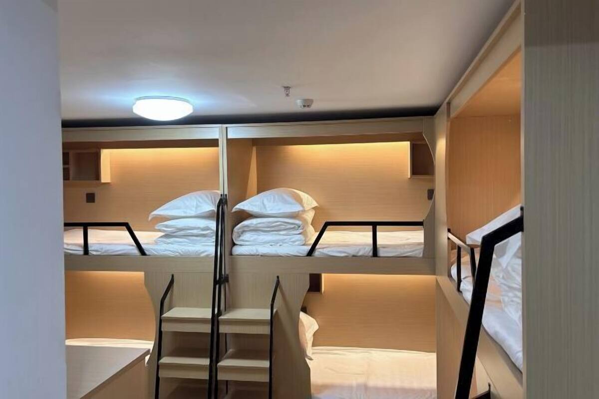 A bunk bed room with a central staircase, wooden walls, and a ceiling light.
