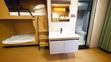 Une chambre d’hôtel de taille réduite, avec des lits superposés, une petite salle de bain et un lavabo.