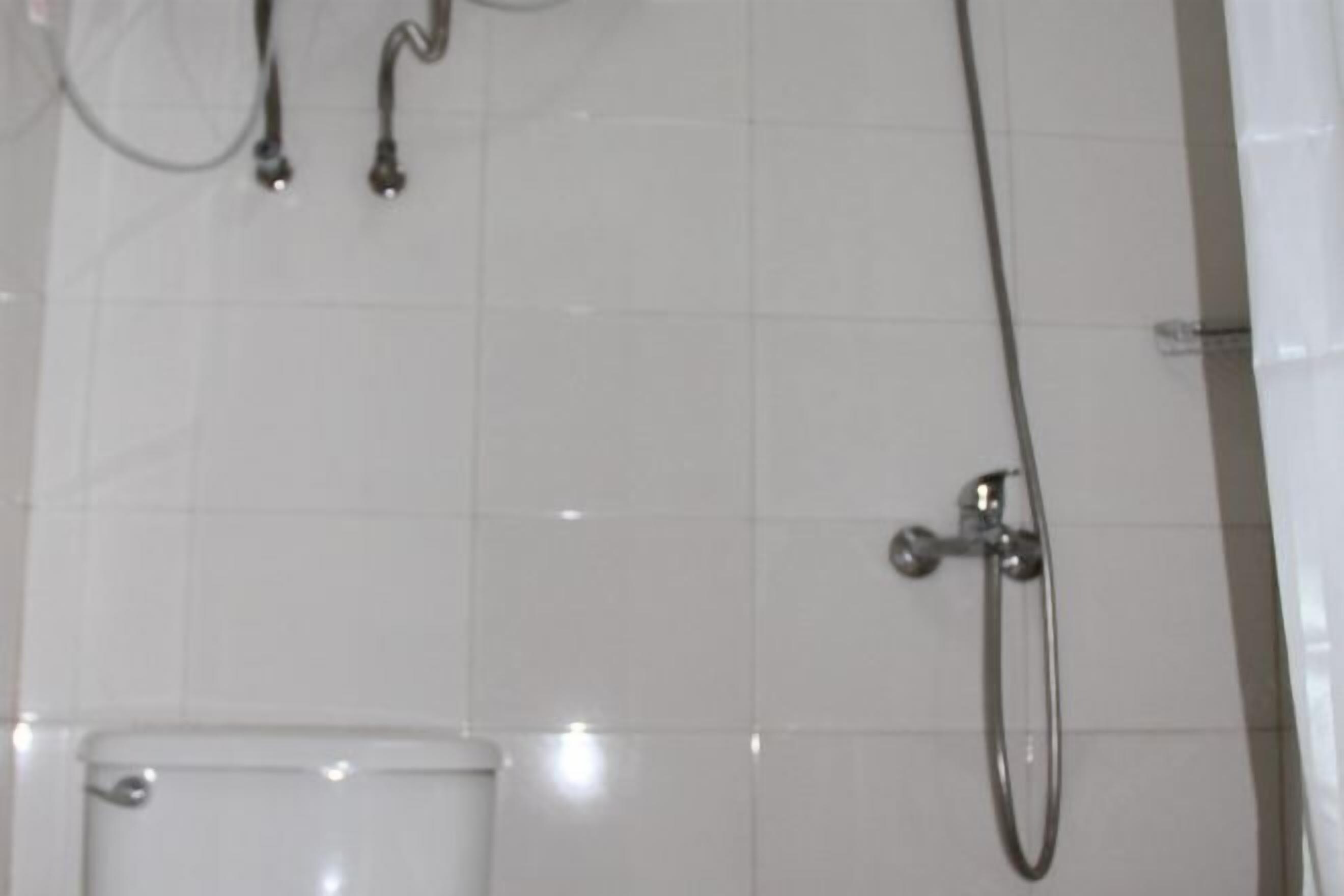 A bathroom with white tiled walls, a toilet, and a shower with a handheld showerhead.