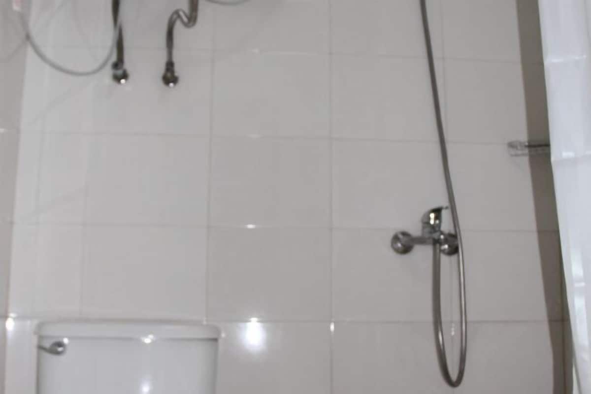A bathroom with white tiled walls, a toilet, and a shower with a handheld showerhead.