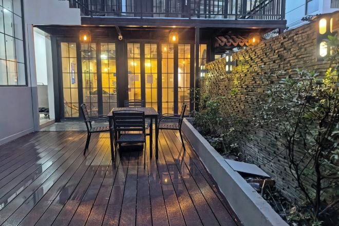 Une terrasse en bois avec une table et des chaises, un mur en briques et une porte vitrée donnant sur un espace intérieur.