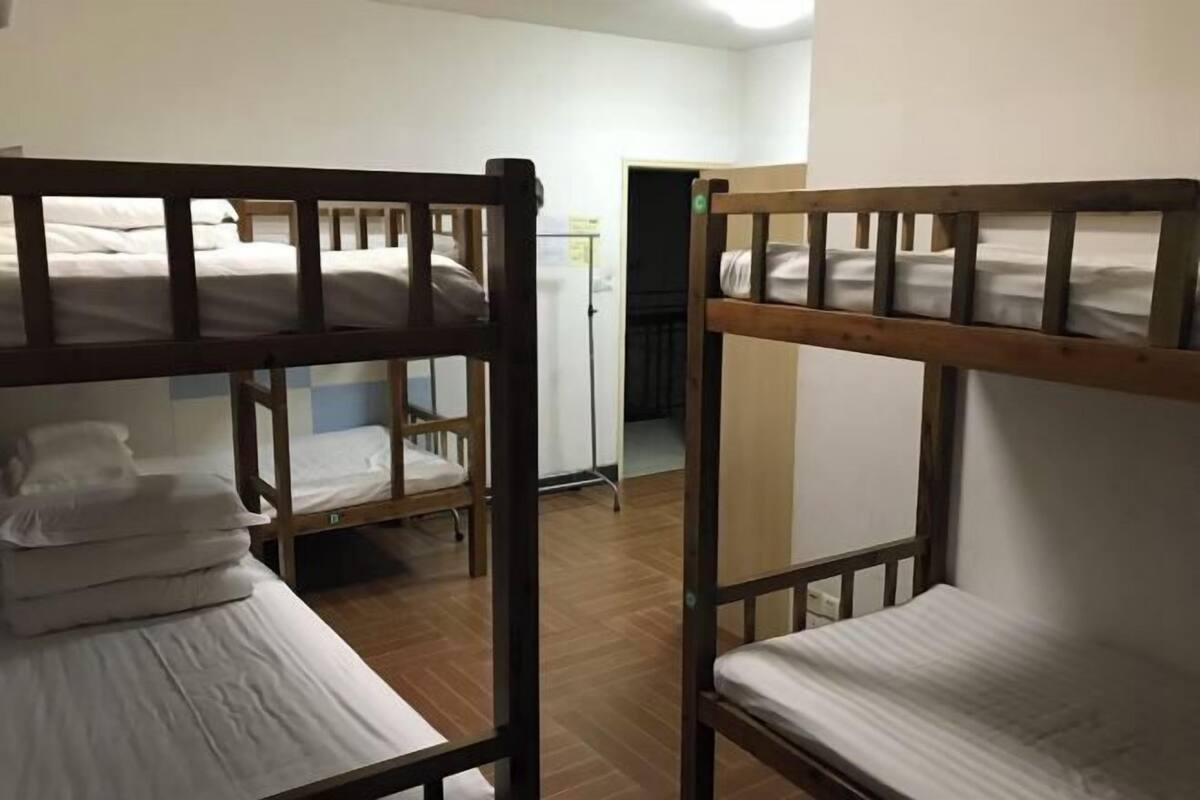 A dormitory room with bunk beds, wooden headboards, and white bedding.