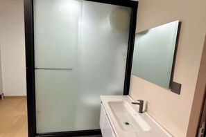 A bathroom with a glass shower enclosure, a white sink, and a mirror. - Beehome Hostel (Shanghai)