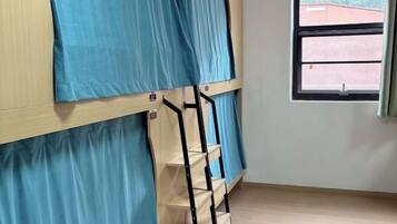 Una cama litera con cortinas azules y una ventana que ofrece vistas a edificios.