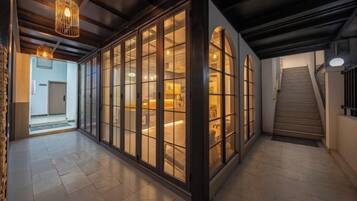 A hallway with a staircase, a wooden floor, and a large glass door leading to a room.