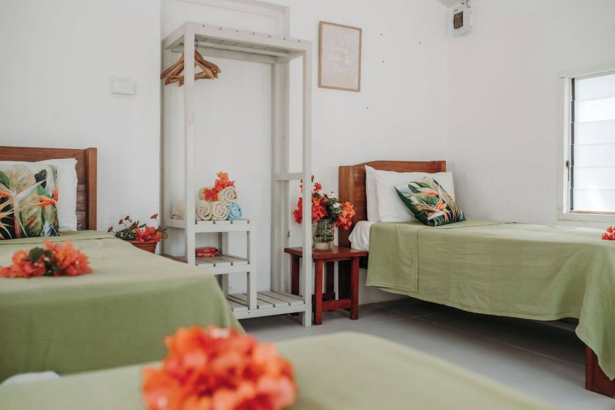 A hotel room with two beds, each with a green bedspread and a wooden headboard. There is a white wardrobe with a mirror and a shelf with decorative items.