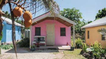 Een klein, roze huis met een witte deur, een bankje en een bloempot voor.