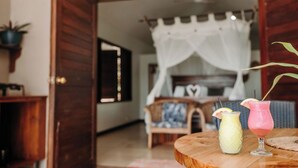 A room with a wooden floor, a bed with a white canopy, and two drinks on a wooden table.